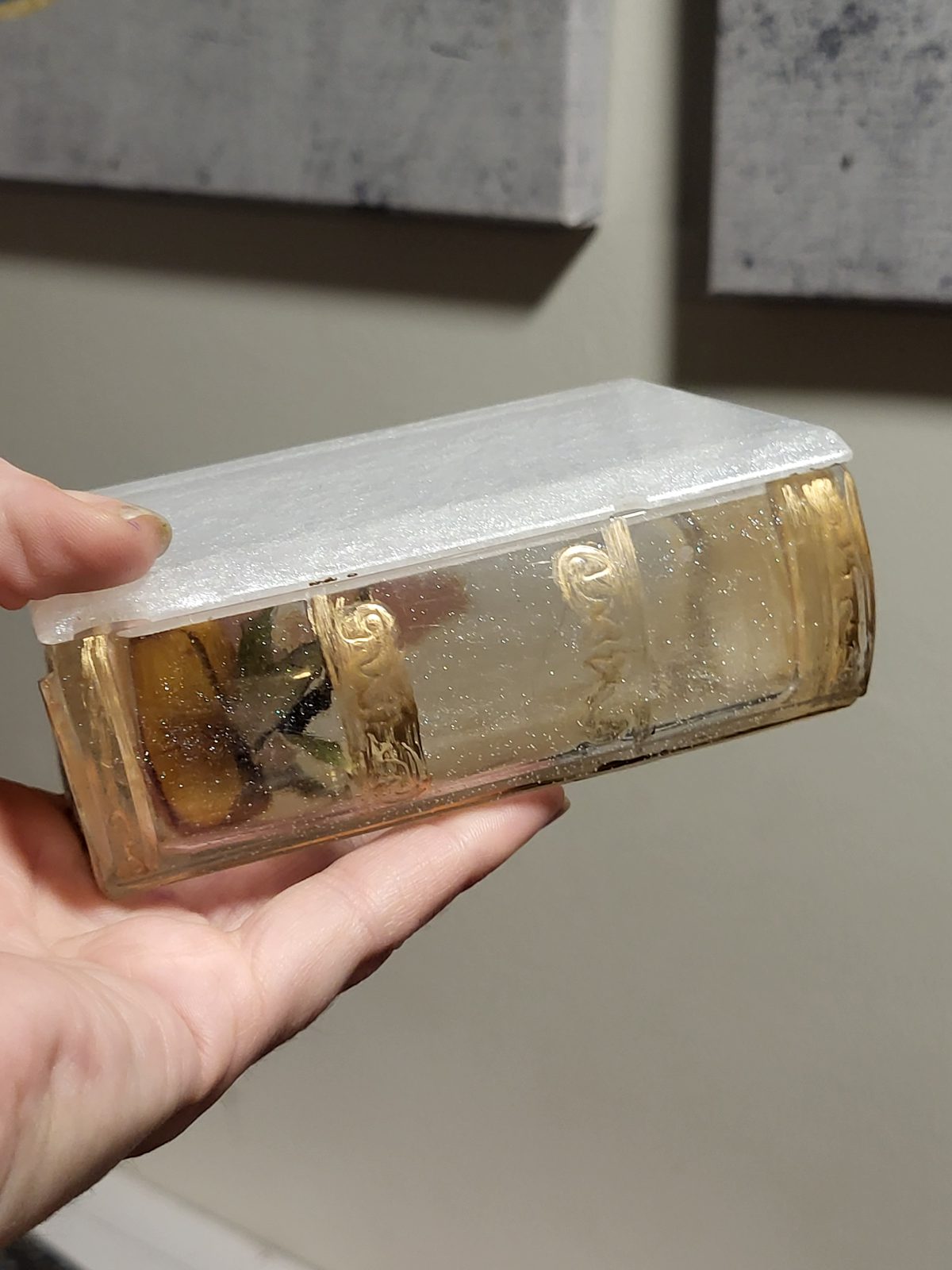 Resin book trinket box held in a hand, showing its pearly white cover and translucent gold-toned spine