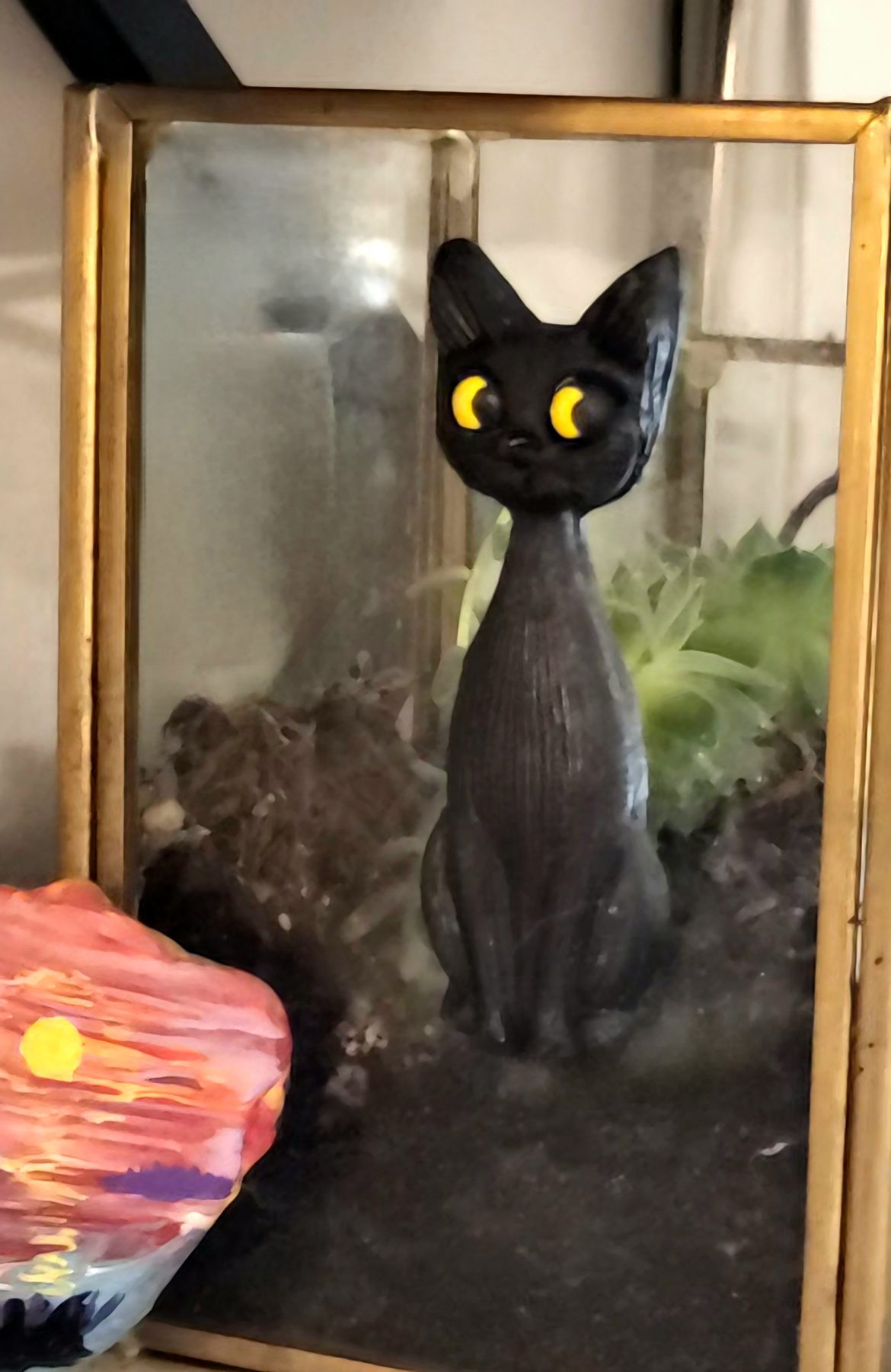 Hand-painted black clay cat with yellow eyes displayed on an antique glass and brass planter