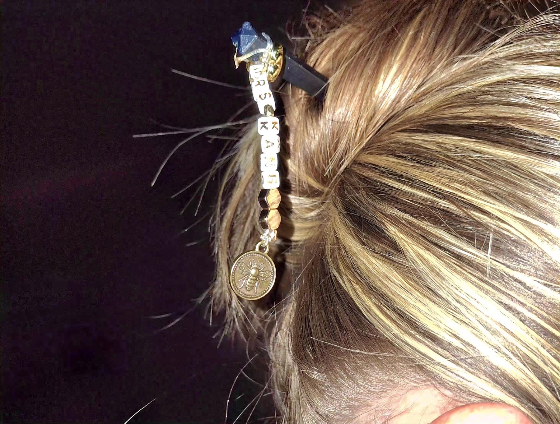 Charm hair accessory with lettered beads and a hanging circular charm, shown worn in hair