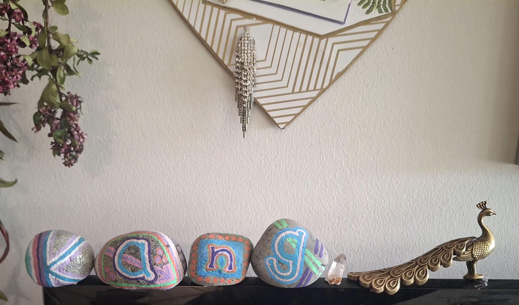 Hand-painted stones spelling Kang displayed together on a shelf