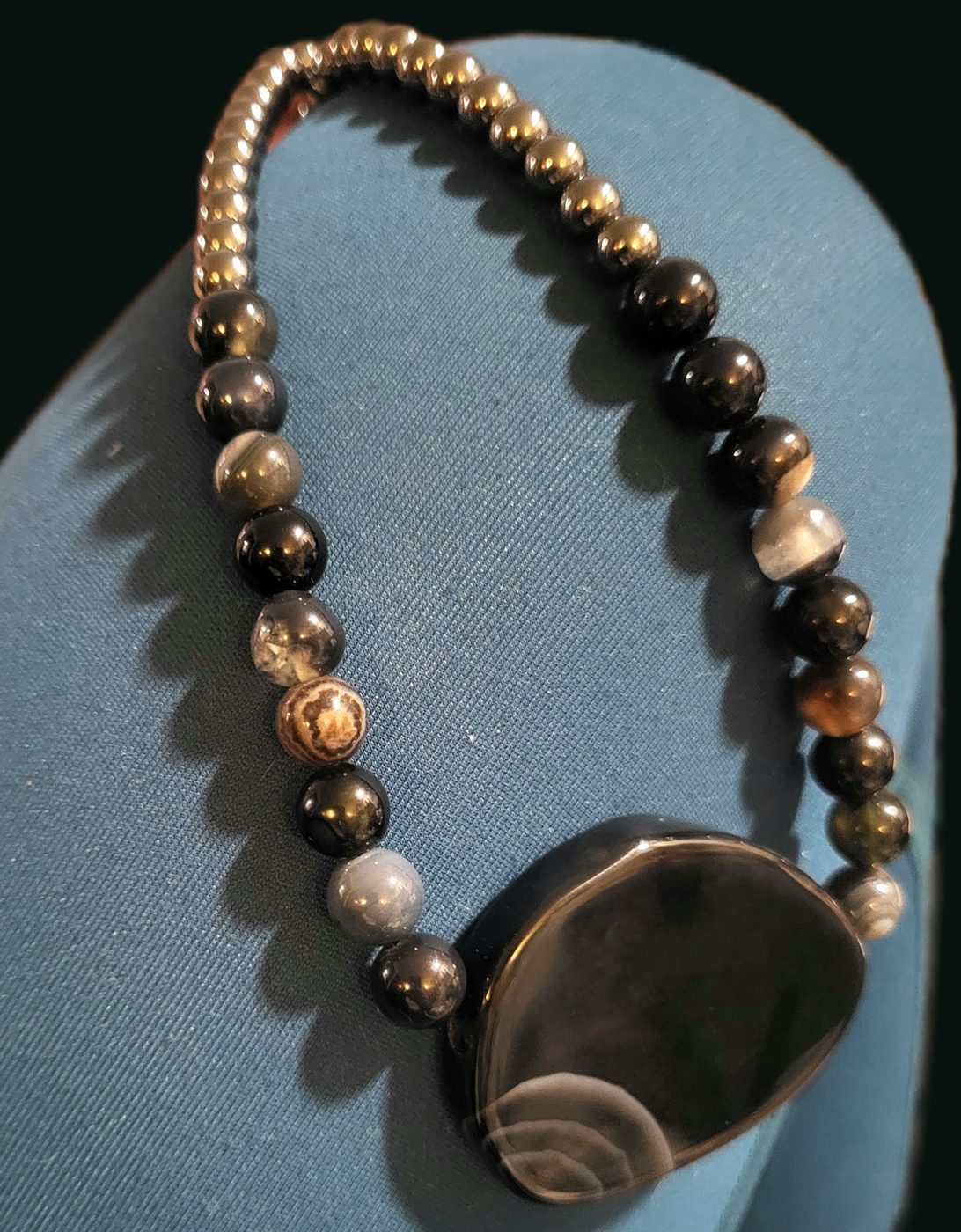 Hematite and banded agate necklace with a large dark banded agate pendant on a blue display bust