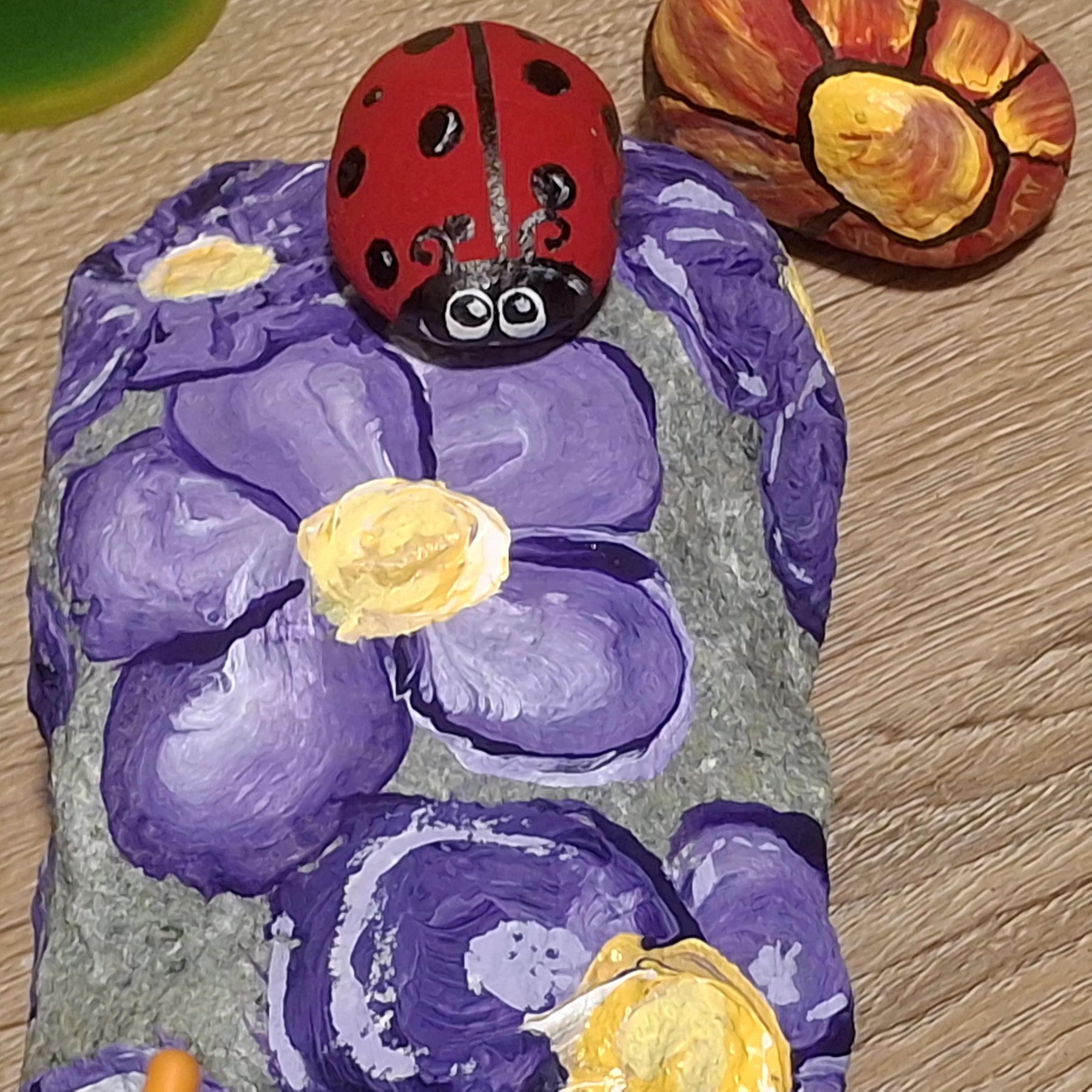 Closer view of a red ladybug and purple flowers on a painted rock