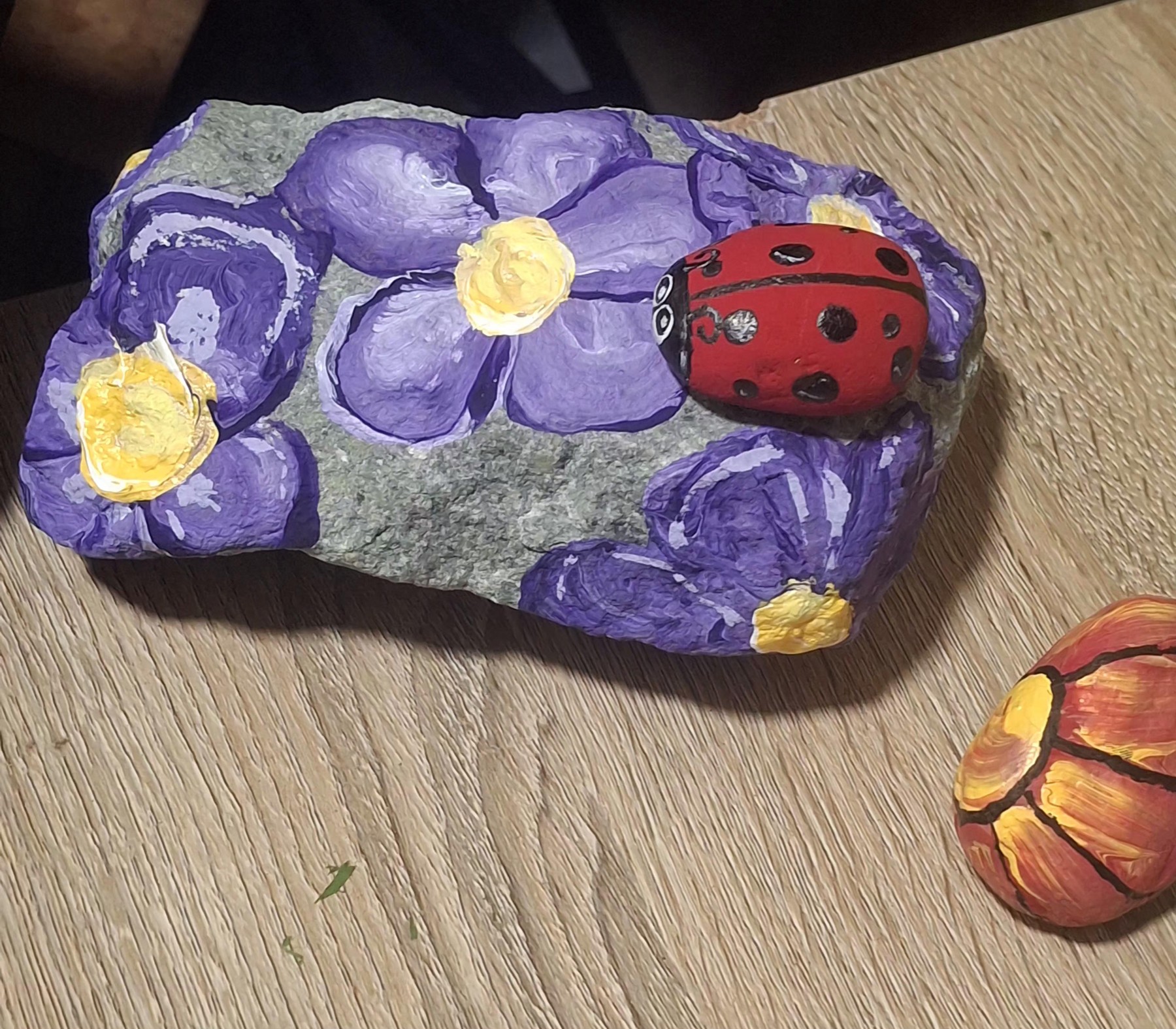 Red hand-painted ladybug sitting on a stone painted with purple flowers