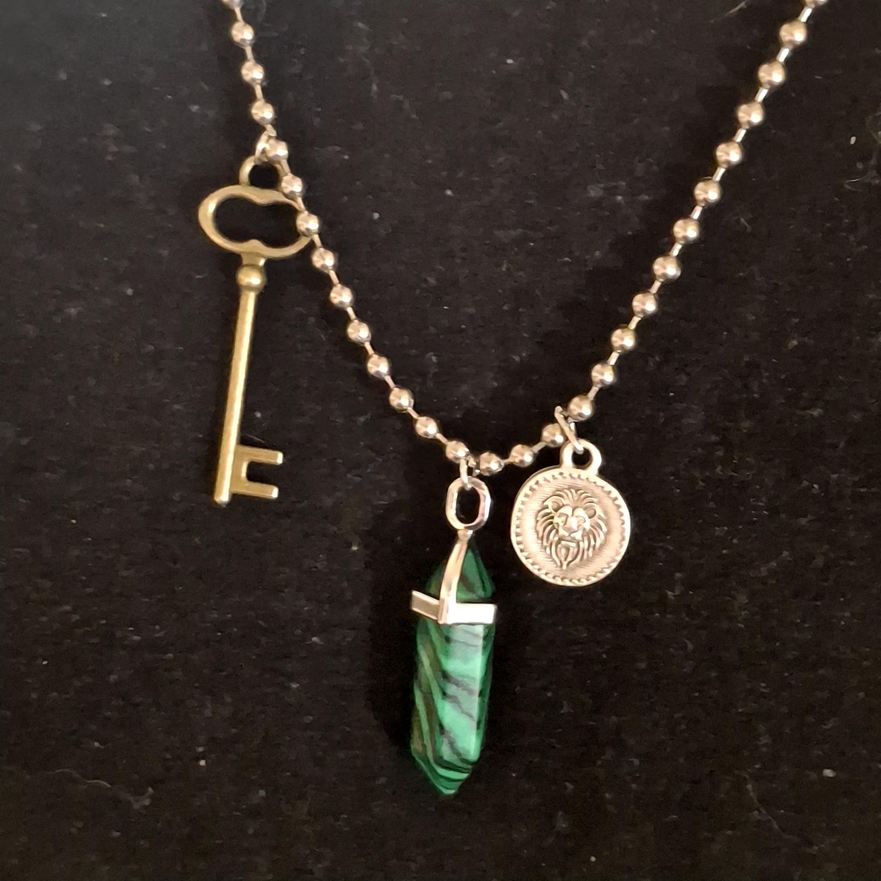 Close view of a necklace with a key charm, lion medallion, and green pendant