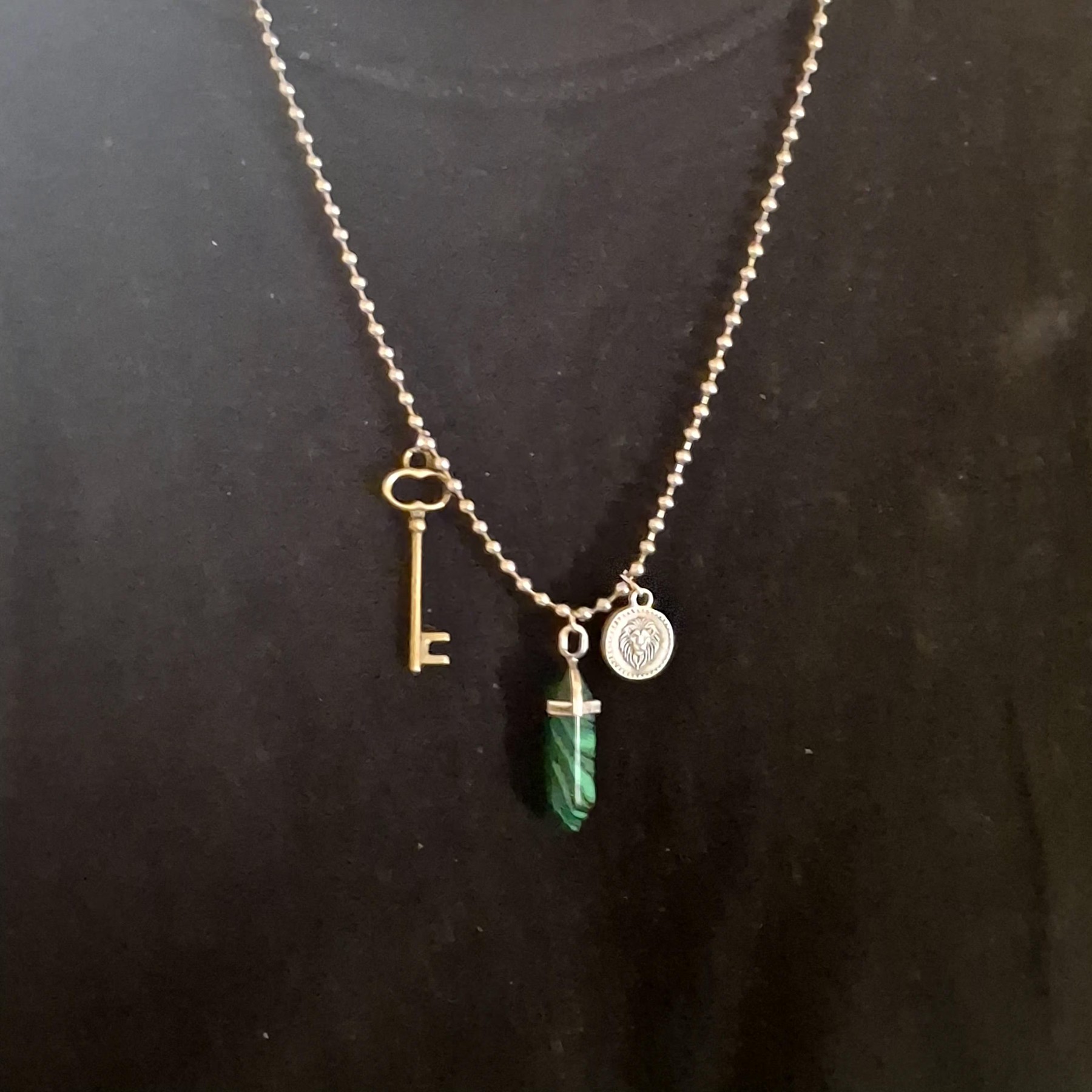 Full view of a necklace with a key charm, lion medallion, and green pendant