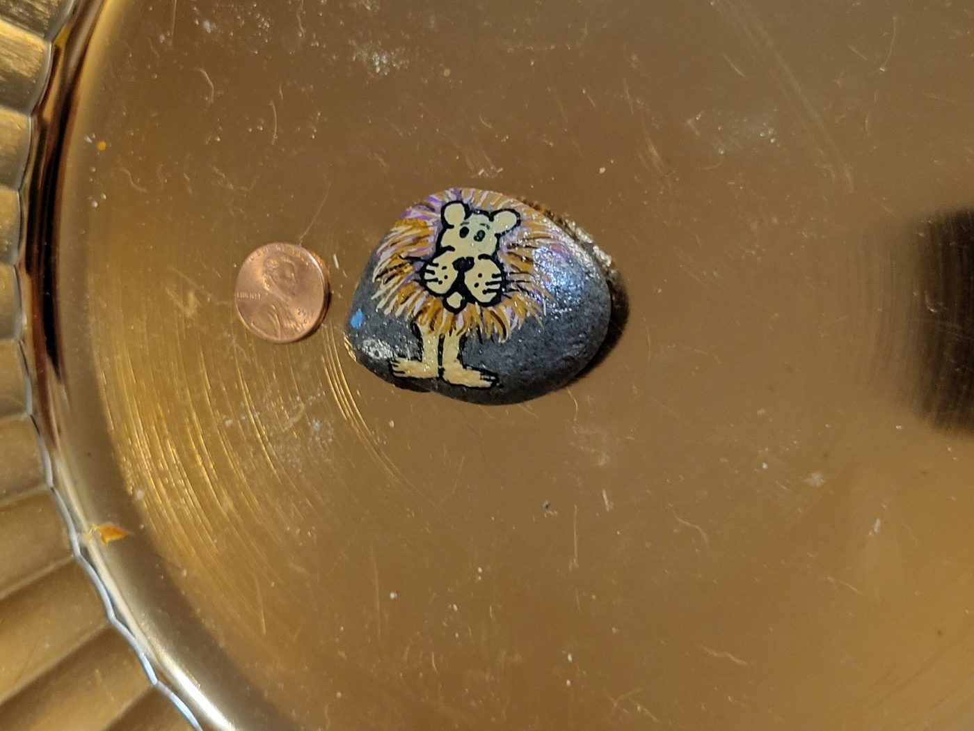 Upright view of the painted lion pebble beside a penny for scale