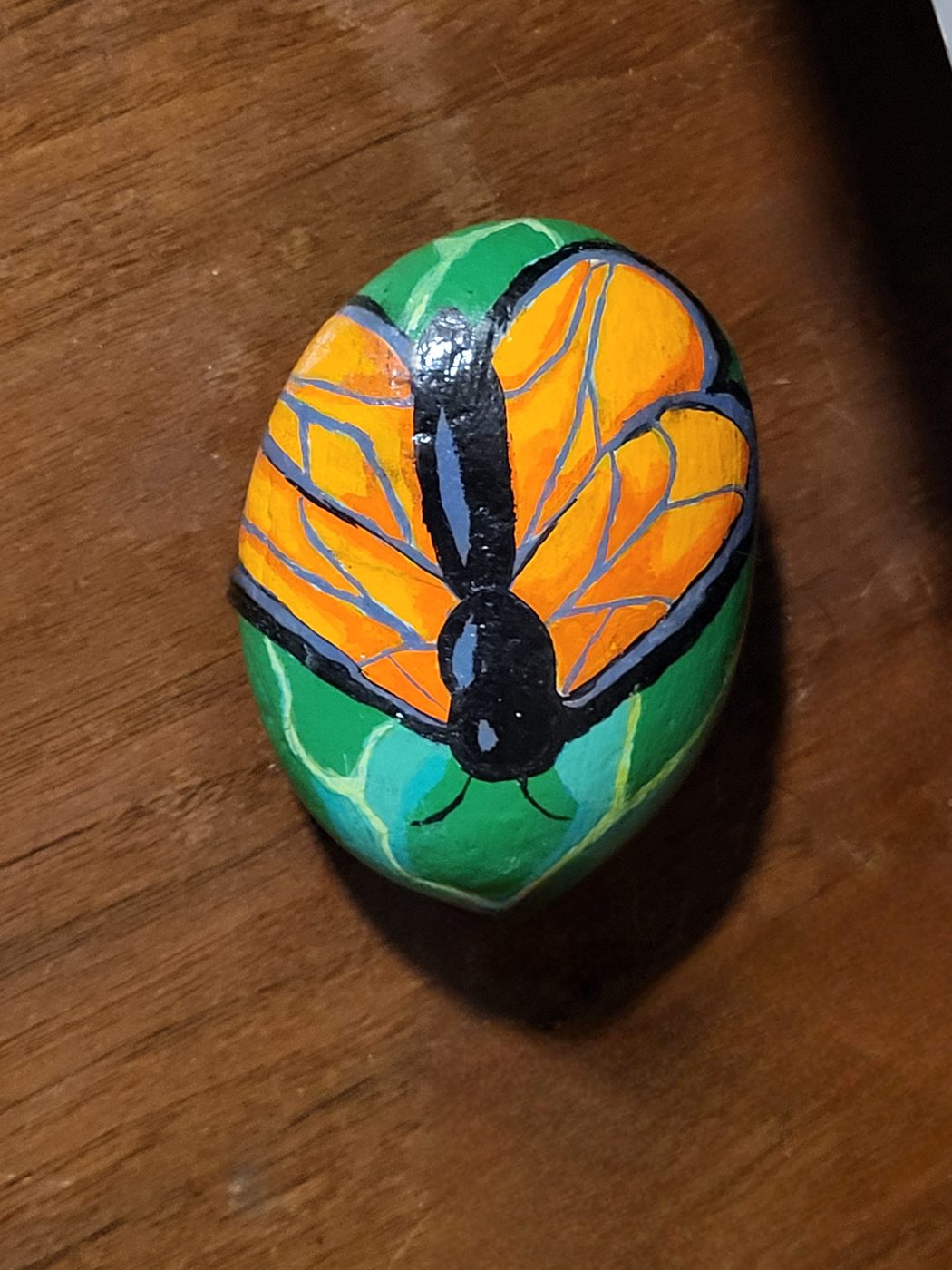 Orange butterfly with detailed black wing lines painted on a green stone