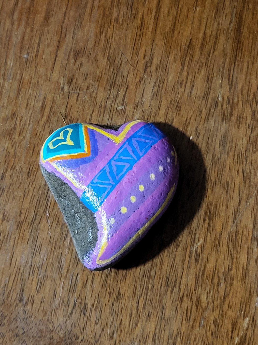 Naturally heart-shaped stone painted with pink and purple geometric patterns