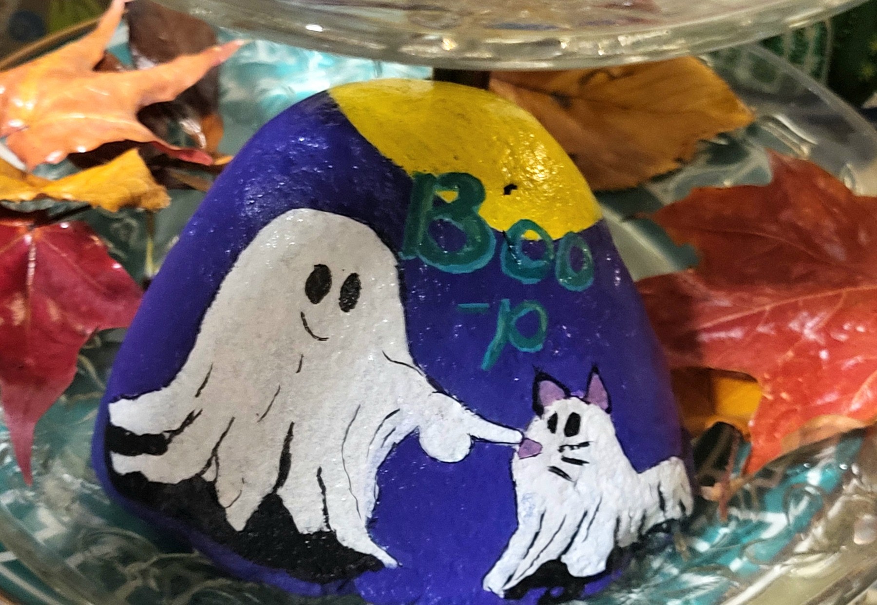 Purple painted rock with a white ghost and ghostly cat beneath a yellow moon