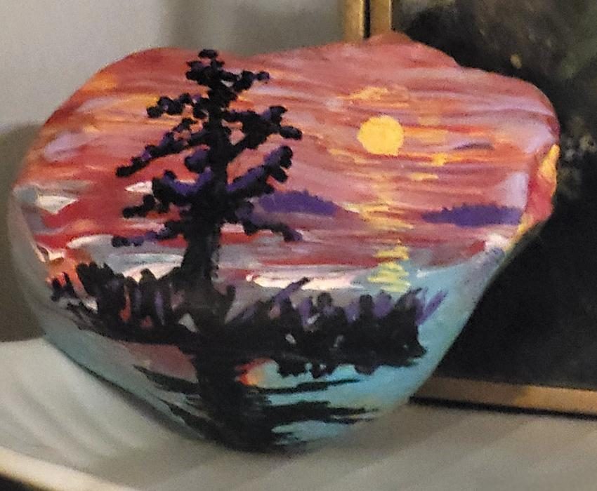 Robin’s hand-painted San Juan Islands sunset rock with a silhouetted evergreen, glowing sky, and reflected light on the water