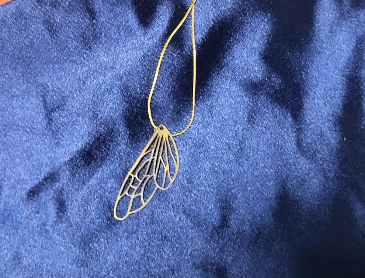 Gold-plated openwork wing pendant on a gold-filled chain, displayed on deep blue fabric