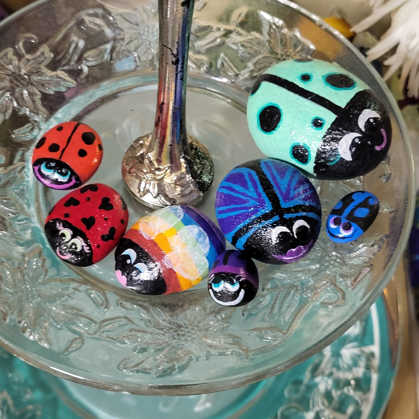 Seven hand-painted ladybug and patterned beetle stones displayed together, showing different sizes, colors, and patterns