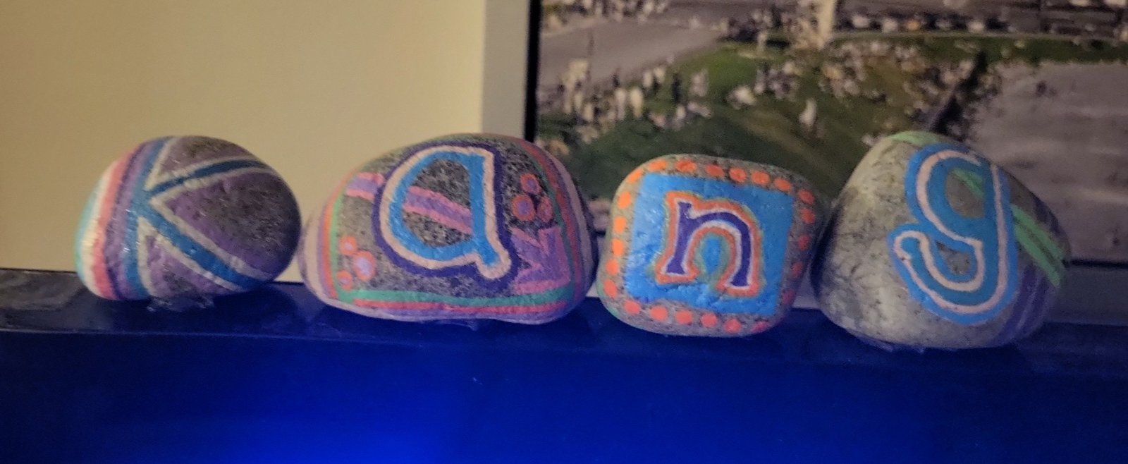 Four individually hand-painted stones spelling Kang, with coordinated colorful lettering and patterns