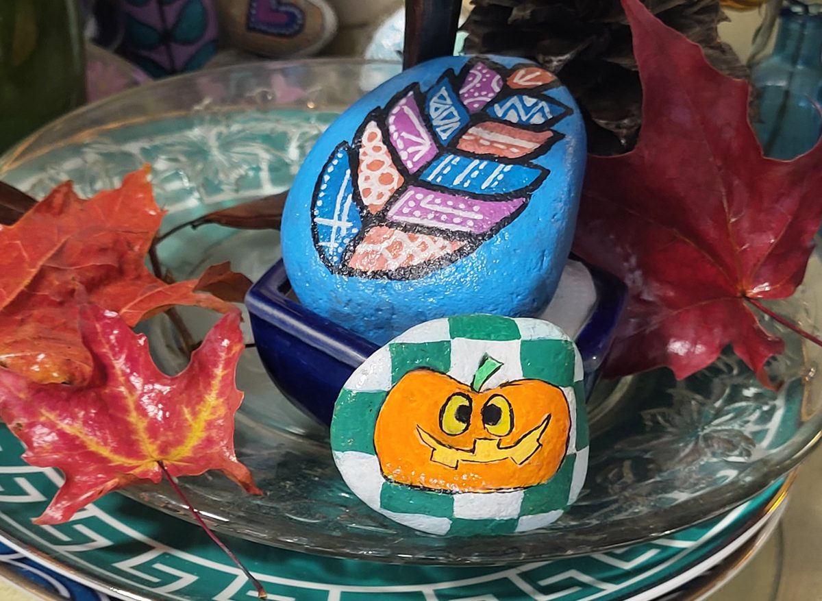 Two painted rocks featuring a patterned autumn leaf and a smiling Halloween pumpkin