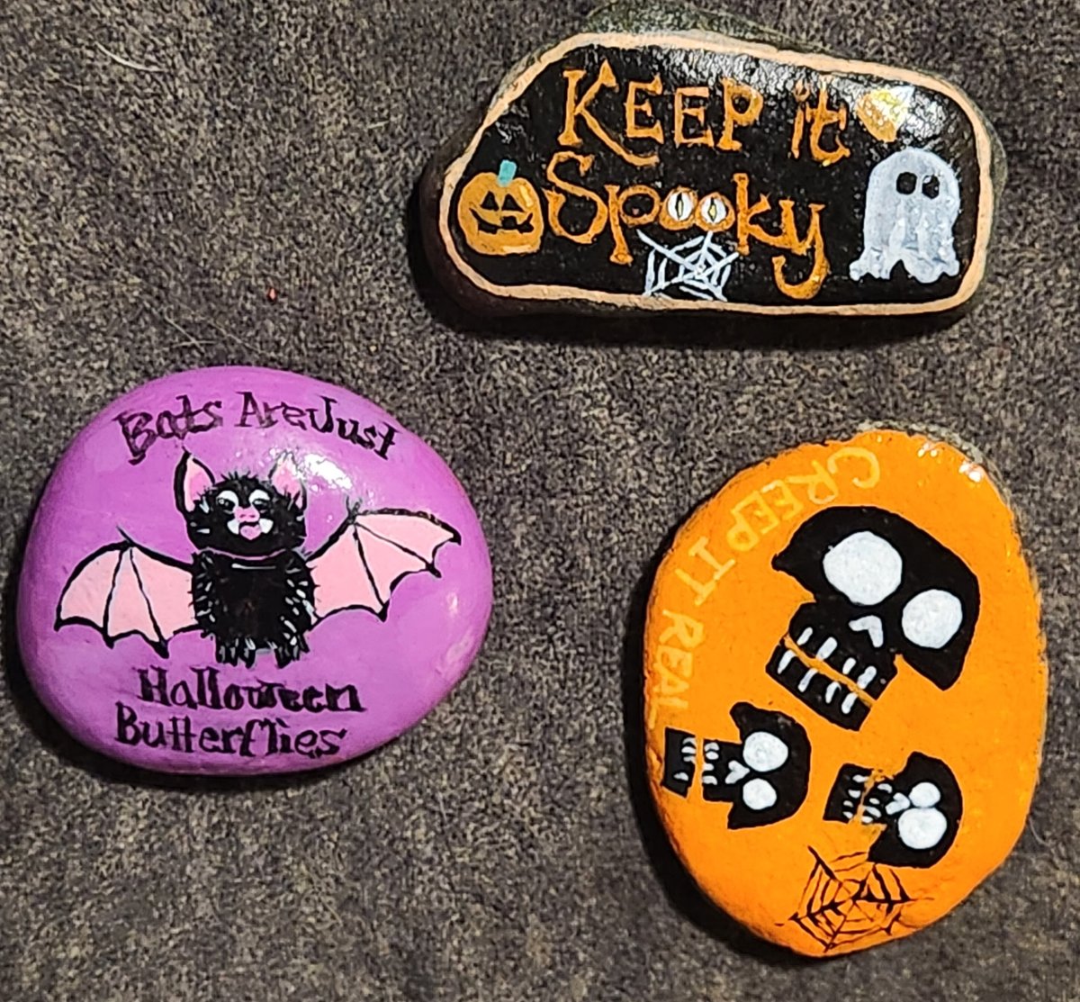 Three Halloween-painted rocks featuring Keep it Spooky, a bat, and skull designs
