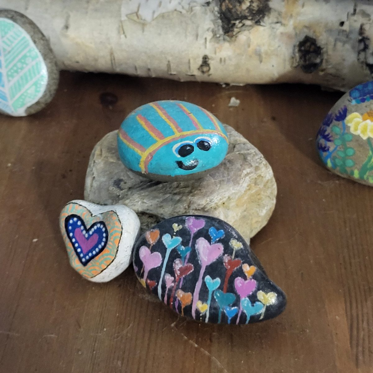 Turquoise beetle with gold stripes displayed with a purple heart stone and a black stone painted with colorful heart-shaped flowers