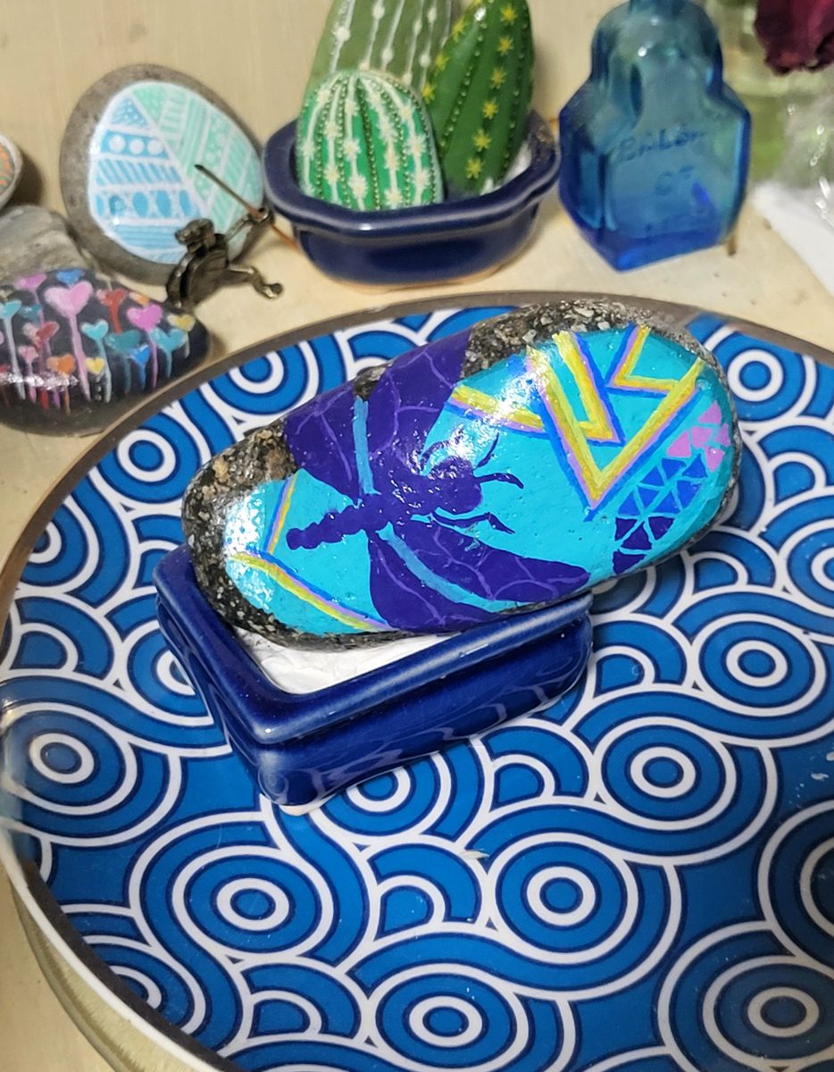 Purple dragonfly surrounded by turquoise and gold geometric patterns on a painted stone