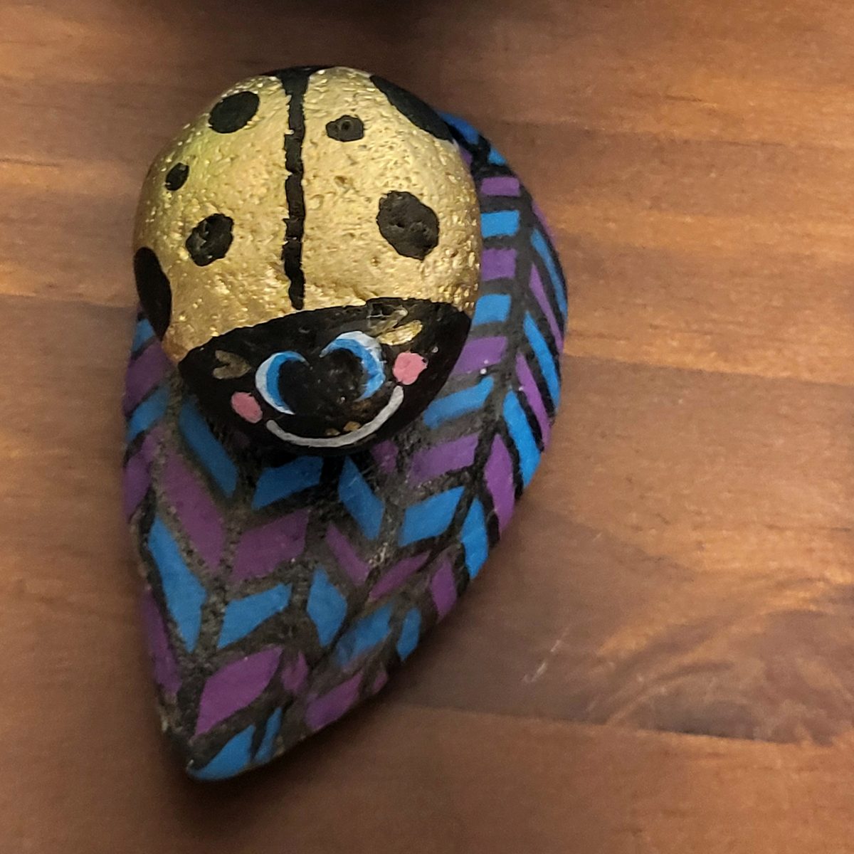 Gold ladybug with blue eyes on a purple-and-blue geometric accent rock