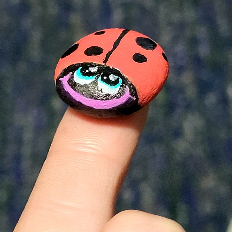 The tiny hand-painted ladybug balanced on a fingertip to show its small size