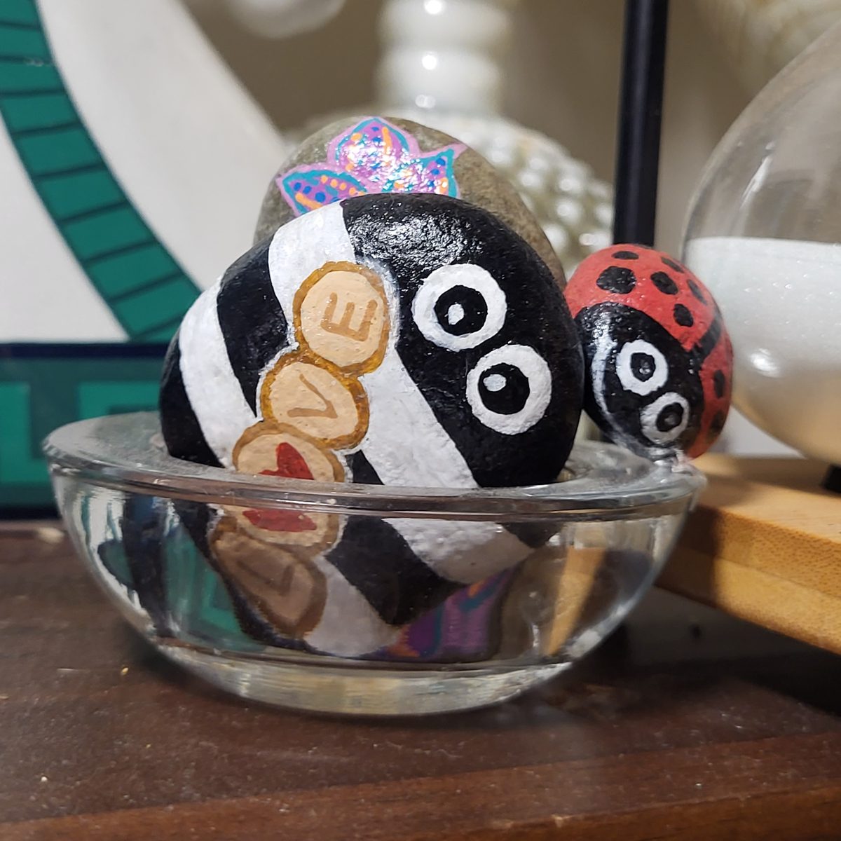 Large black-and-white love bug with LOVE lettering beside a small red ladybug with wide playful eyes, displayed in a glass dish