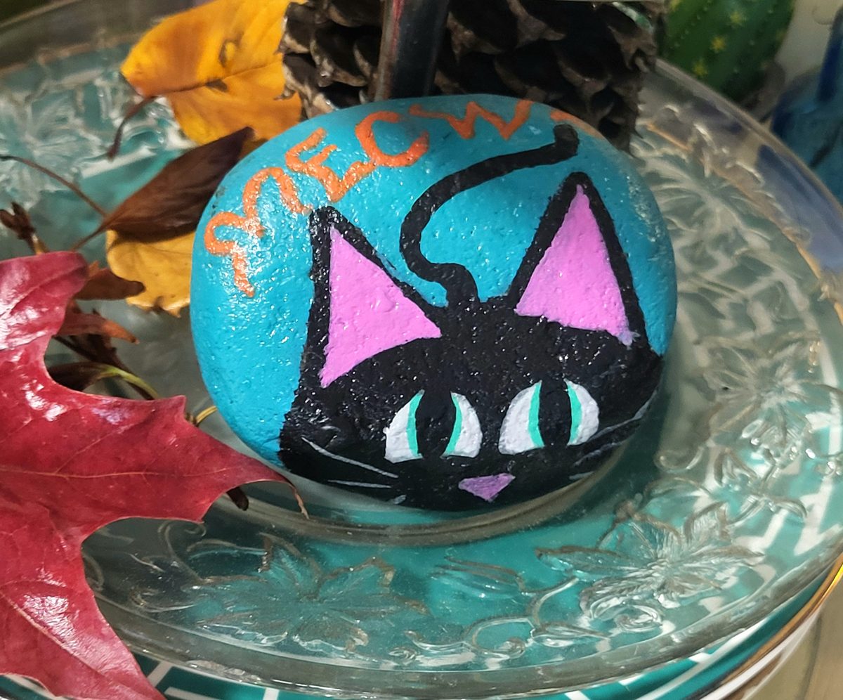 Black cat with green eyes peeking over a painted edge on a turquoise stone