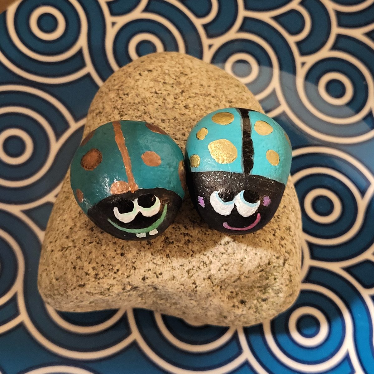 Two teal ladybugs with metallic spots, different eyes, and gentle smiling expressions