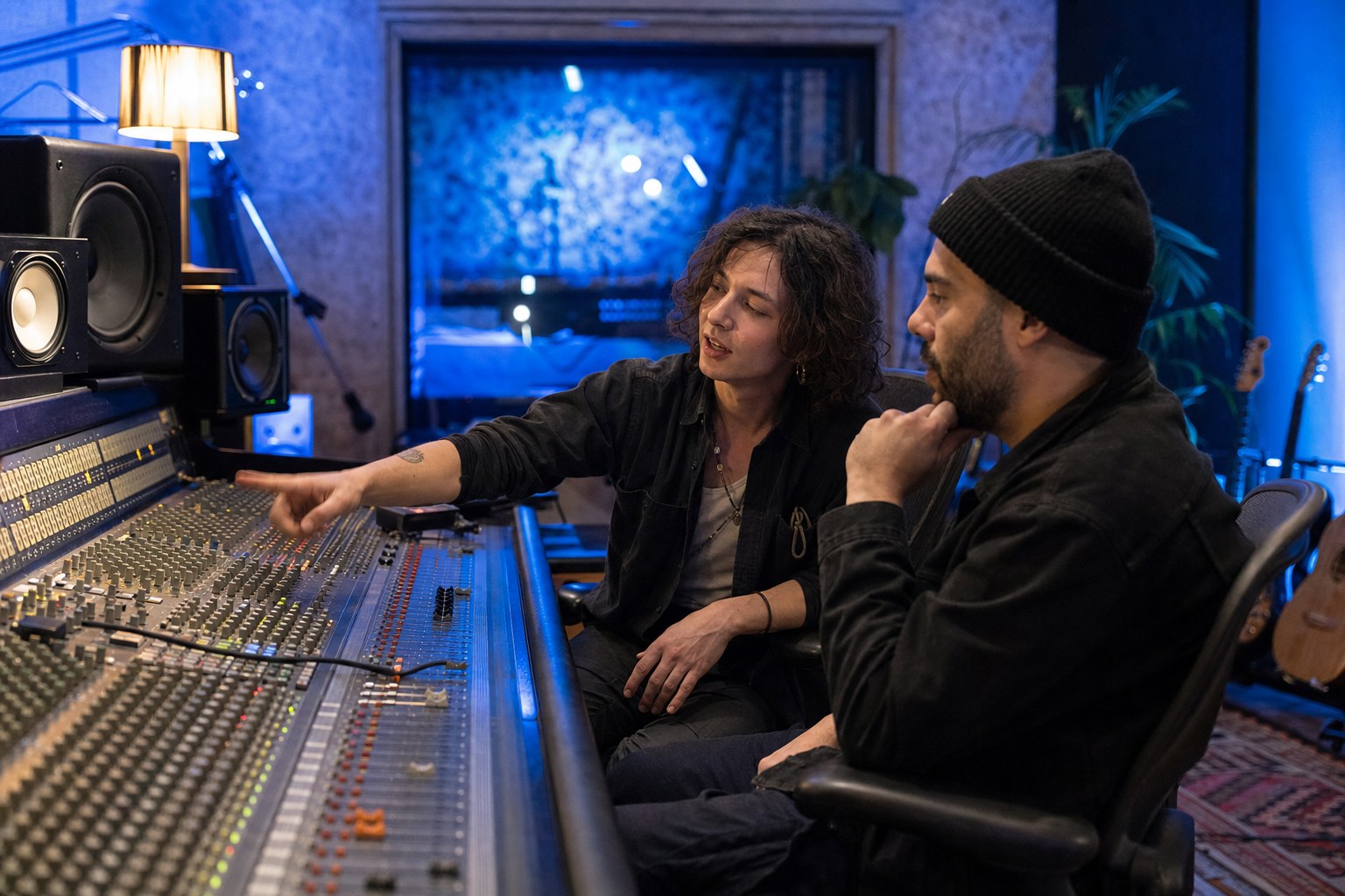 Two musicians listening to a track and discussing a mixing console in a recording studio
