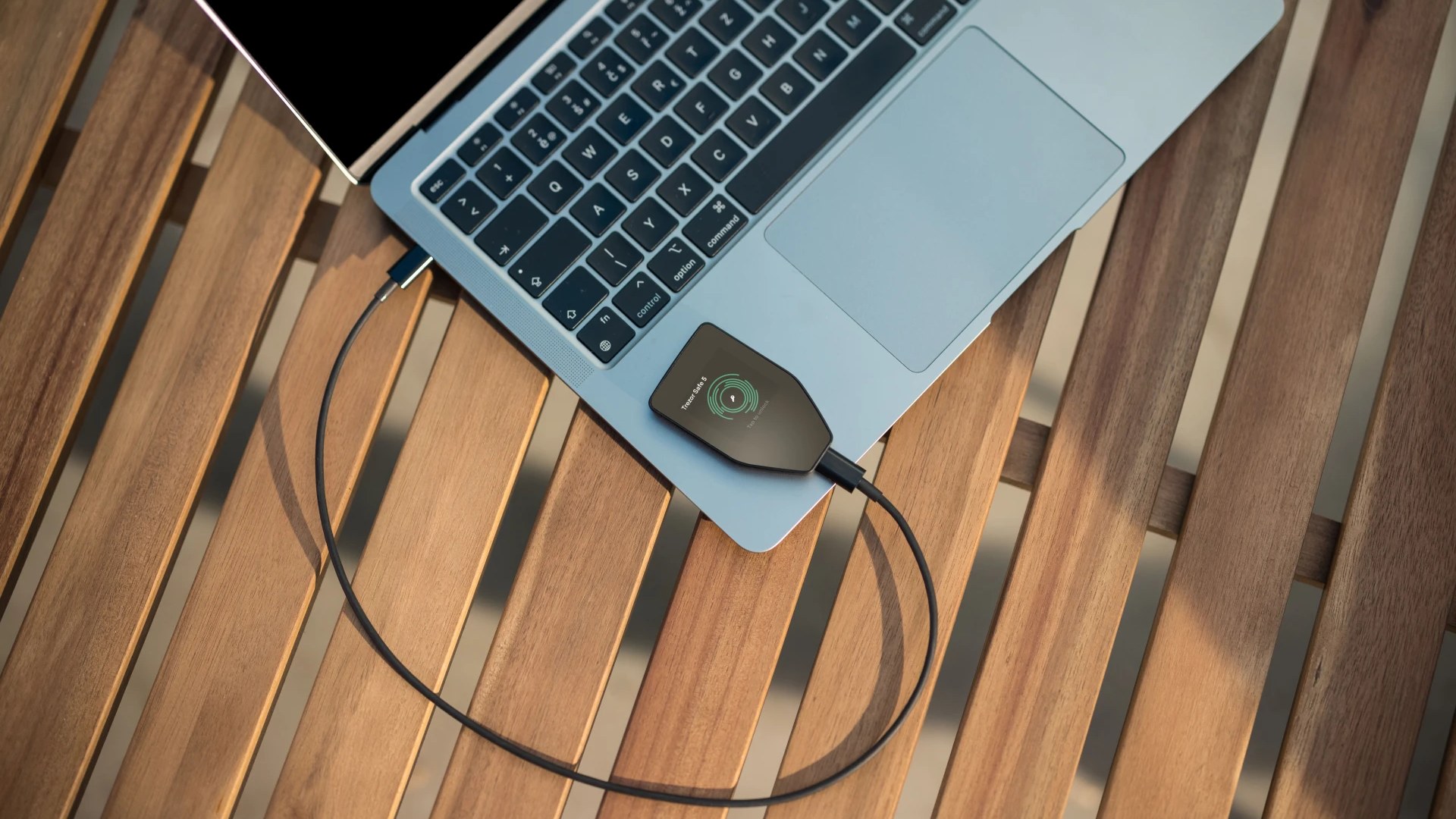 A Trezor Safe 5 connected to a laptop on a wood table