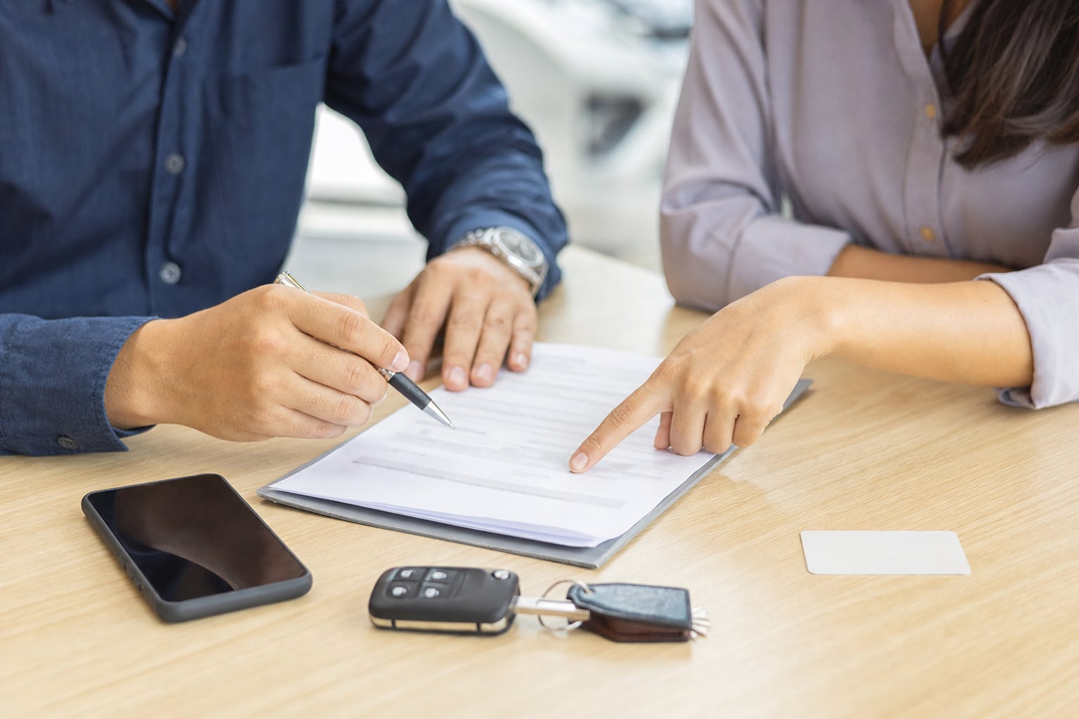 Two people reviewing a rental agreement with a car key and phone on the counter
