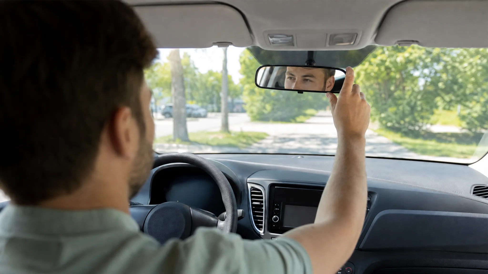 Driver adjusting the rear-view mirror before leaving in a rental car