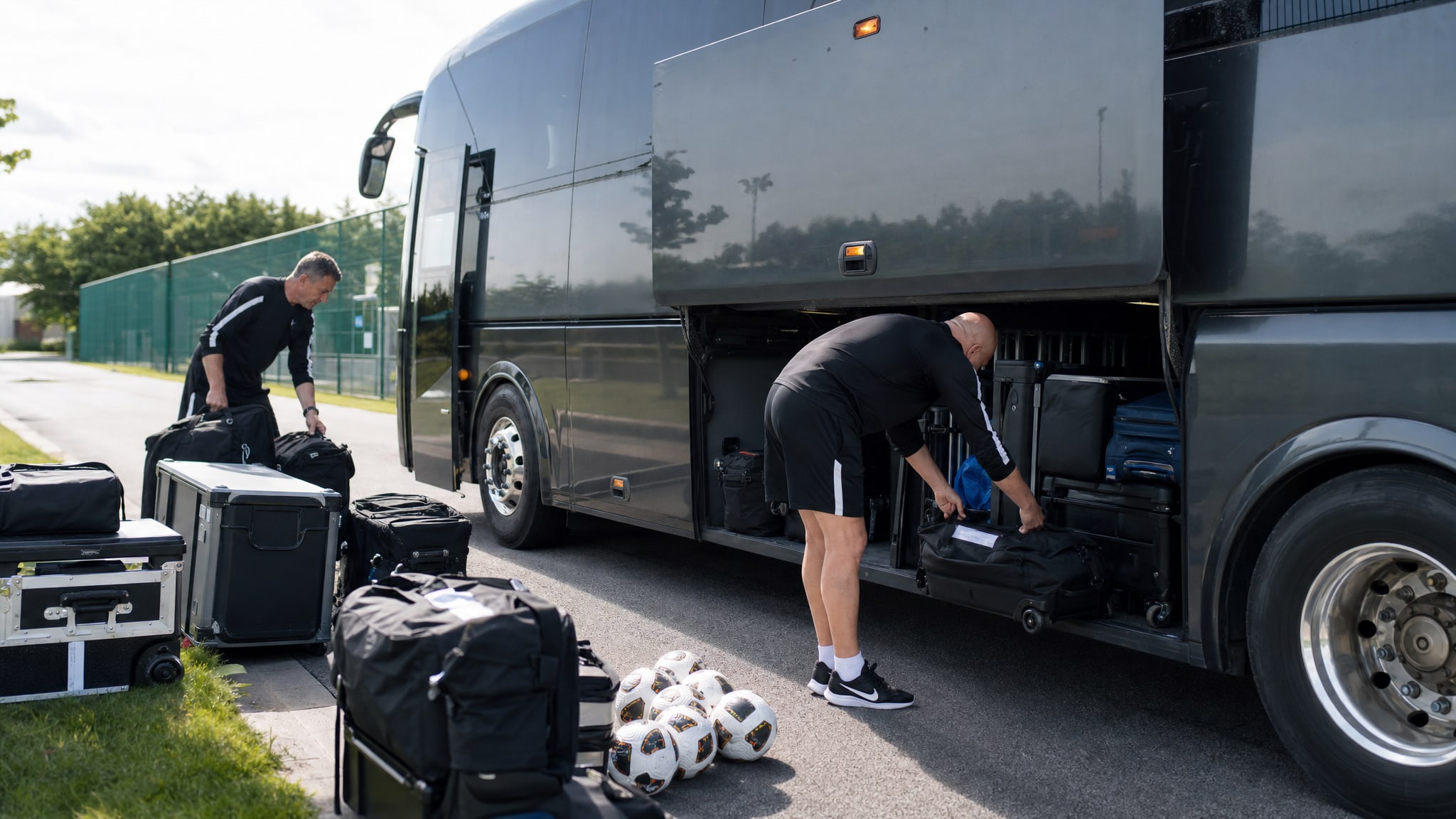Football operations staff loading equipment cases and training balls into a team coach