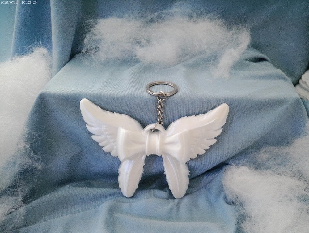 A handmade white angel wings keychain with a bow