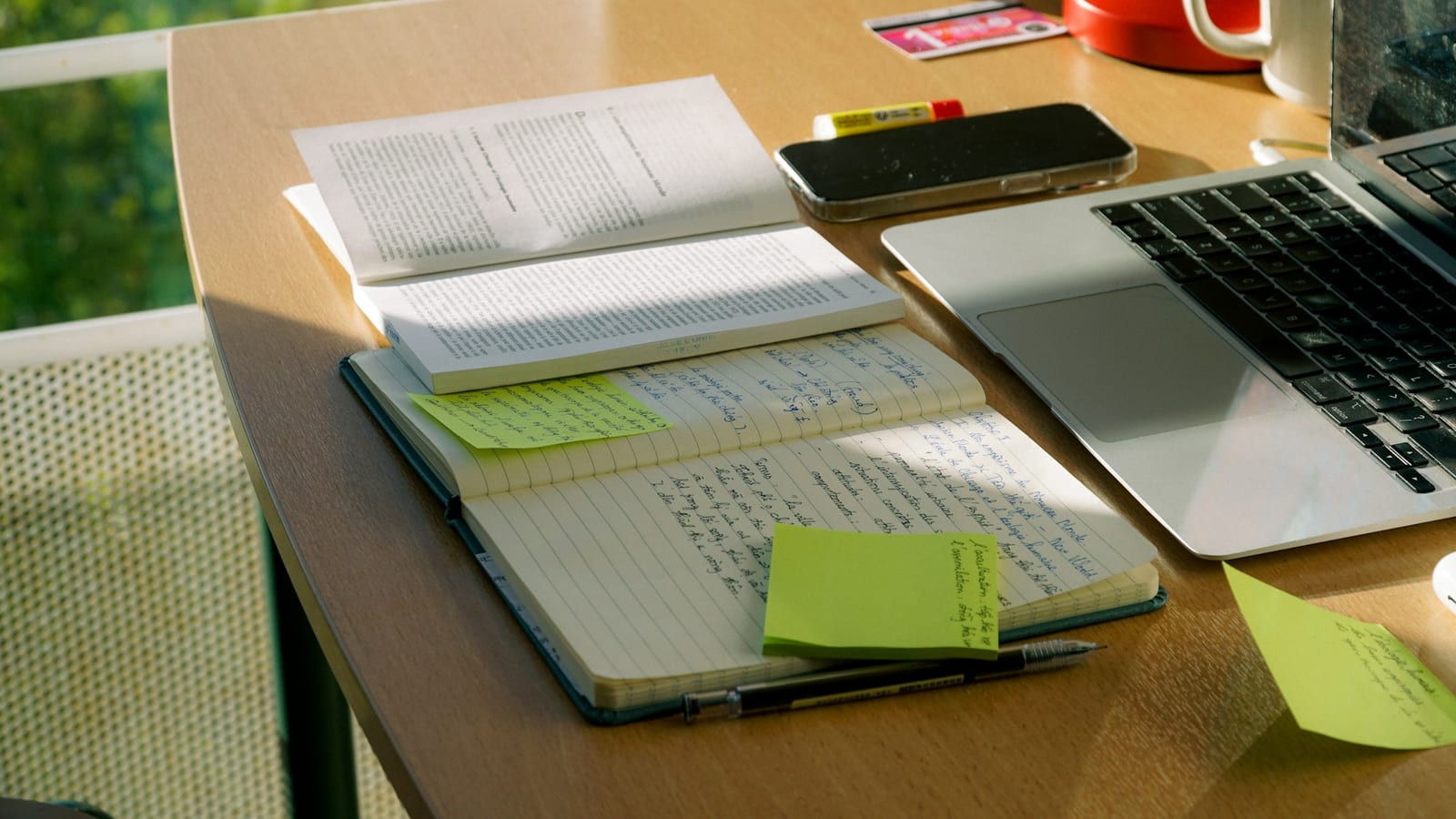 Notebook and laptop on a sunlit desk