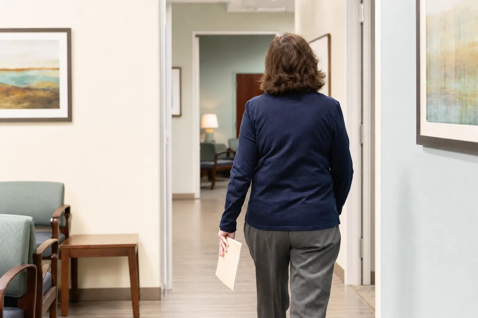 Person carrying a plain folder through a neutral outpatient office hallway