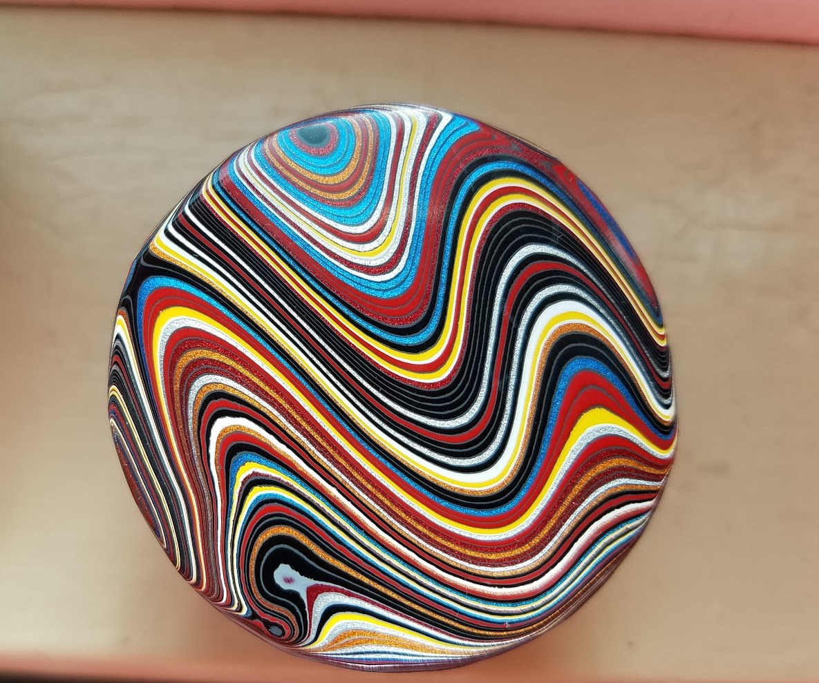 Polished Fordite cabochon with flowing red, blue, yellow, and white layers