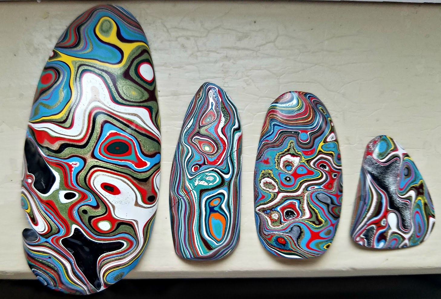 Four polished Fordite pieces with colorful automotive paint layers
