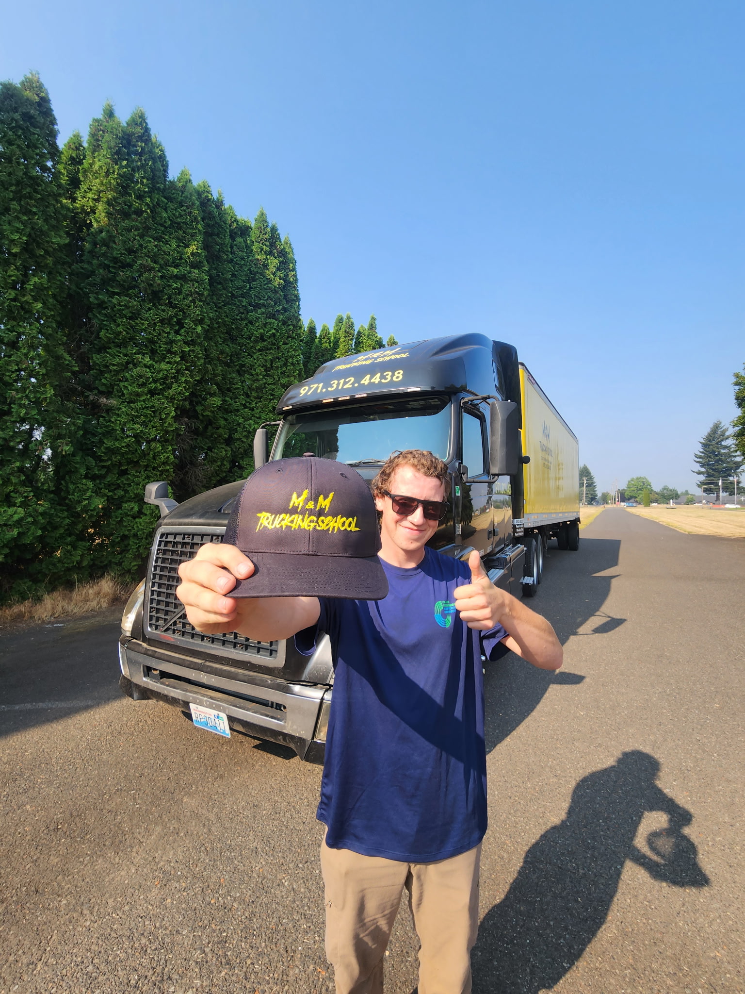 M&M Trucking School graduate holding an M&M cap beside a training truck