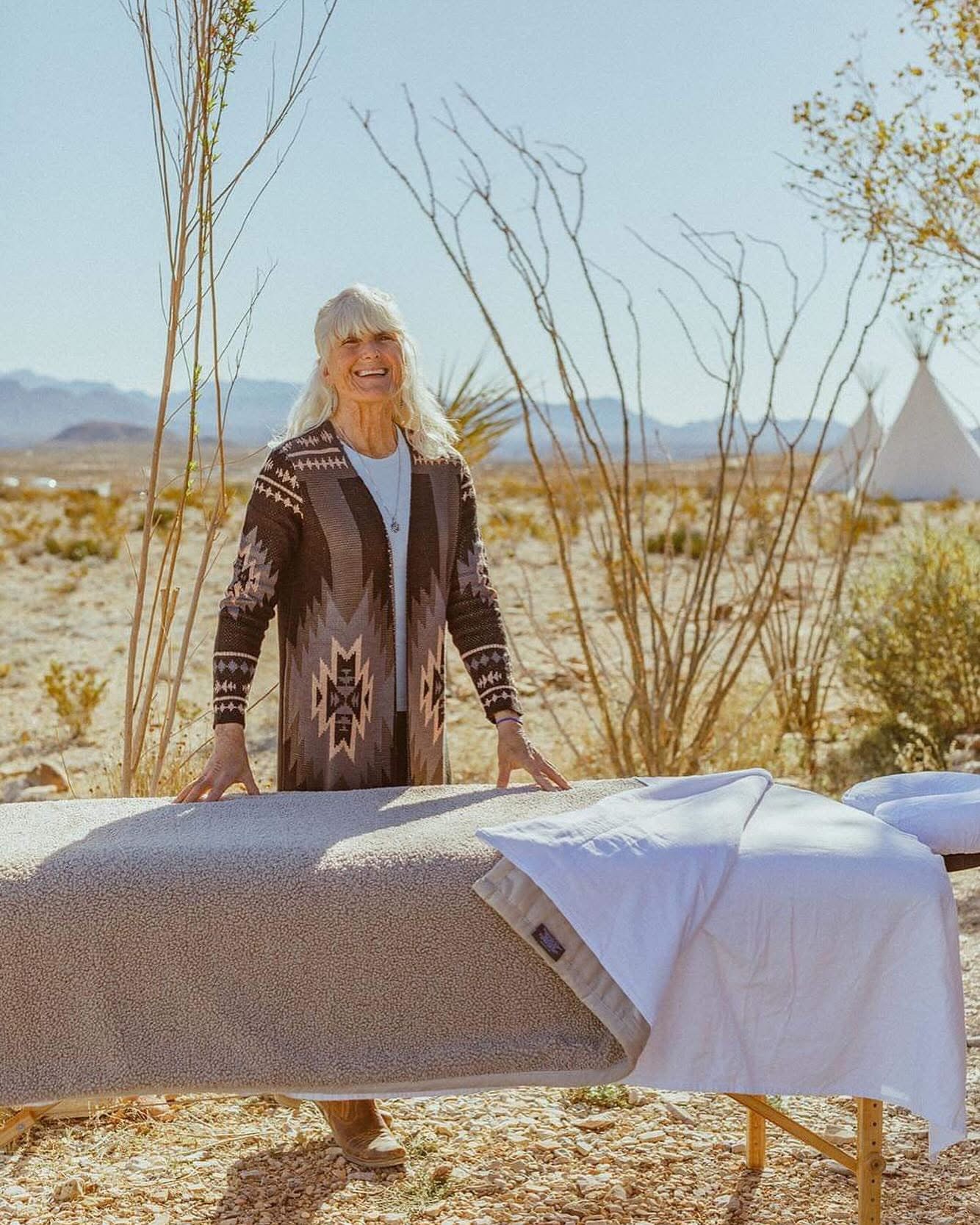 Kate Healy, LMT smiling behind a bodywork table in a desert landscape