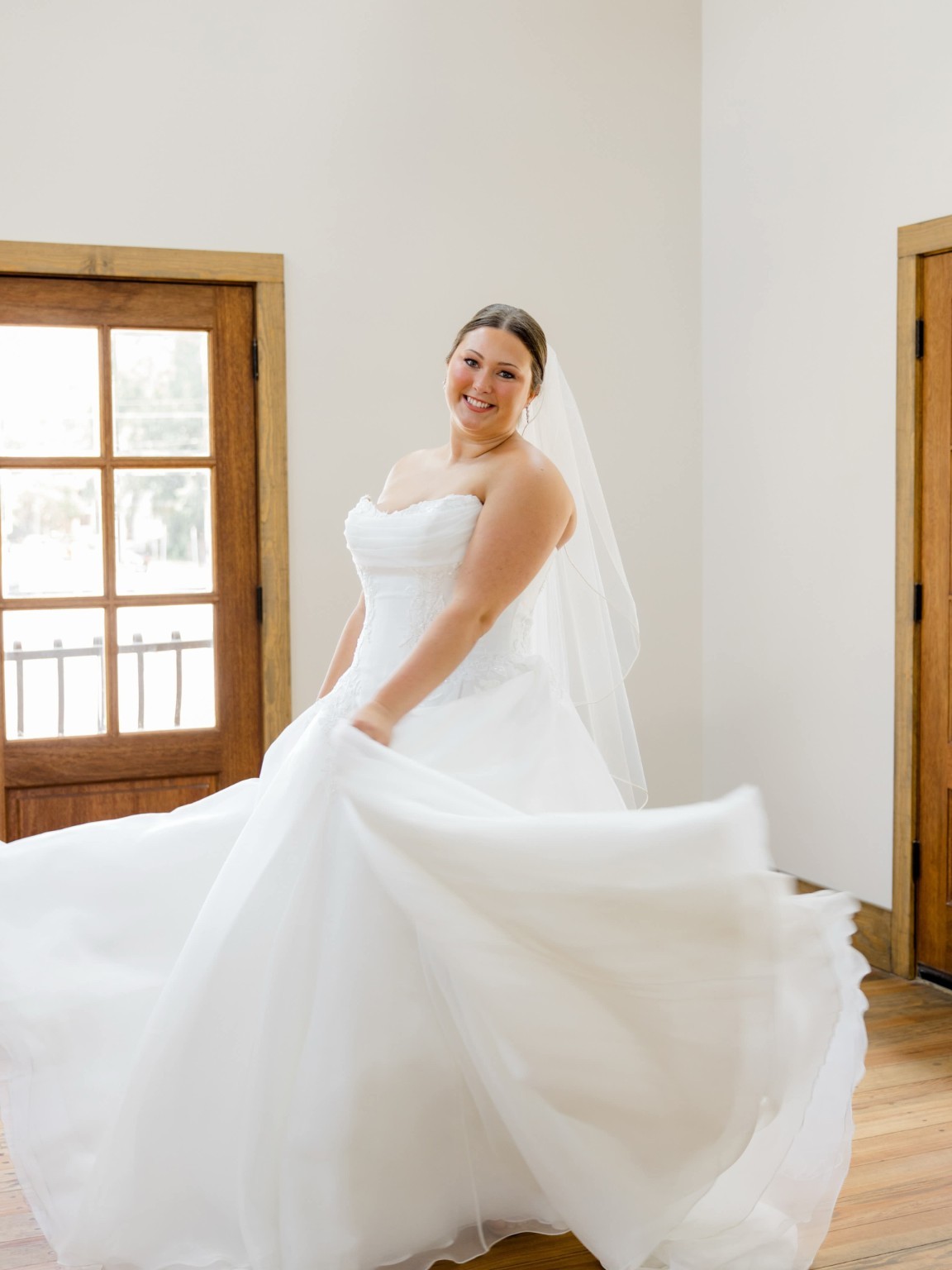 Smiling bride in an elegant updo and veil twirling her wedding gown