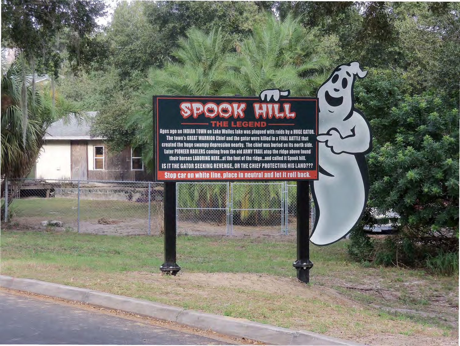 Ghost-shaped Spook Hill sign displaying the alligator legend beside the road in 2018