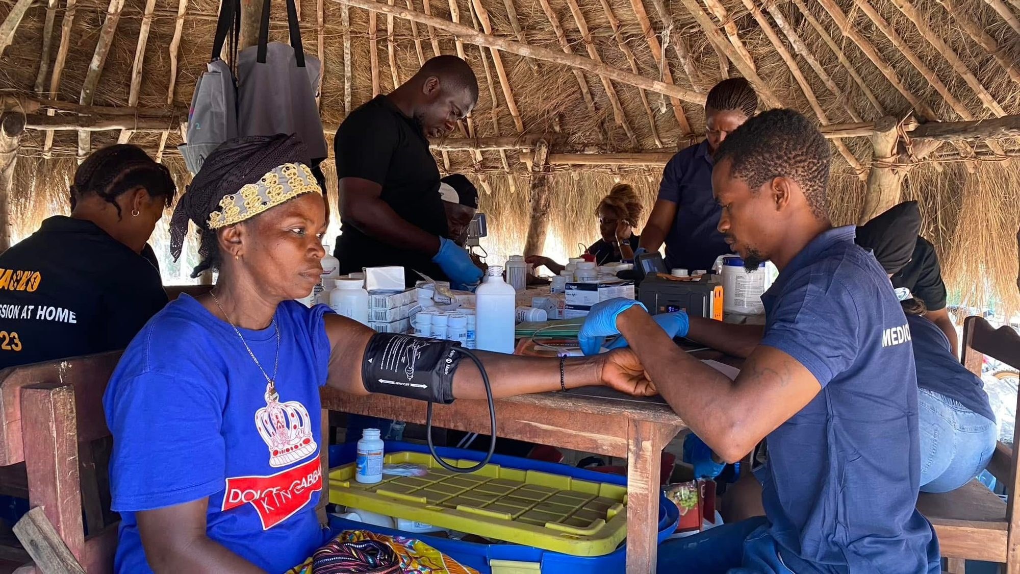 A MaCHO team member checking blood pressure under a thatched shelter