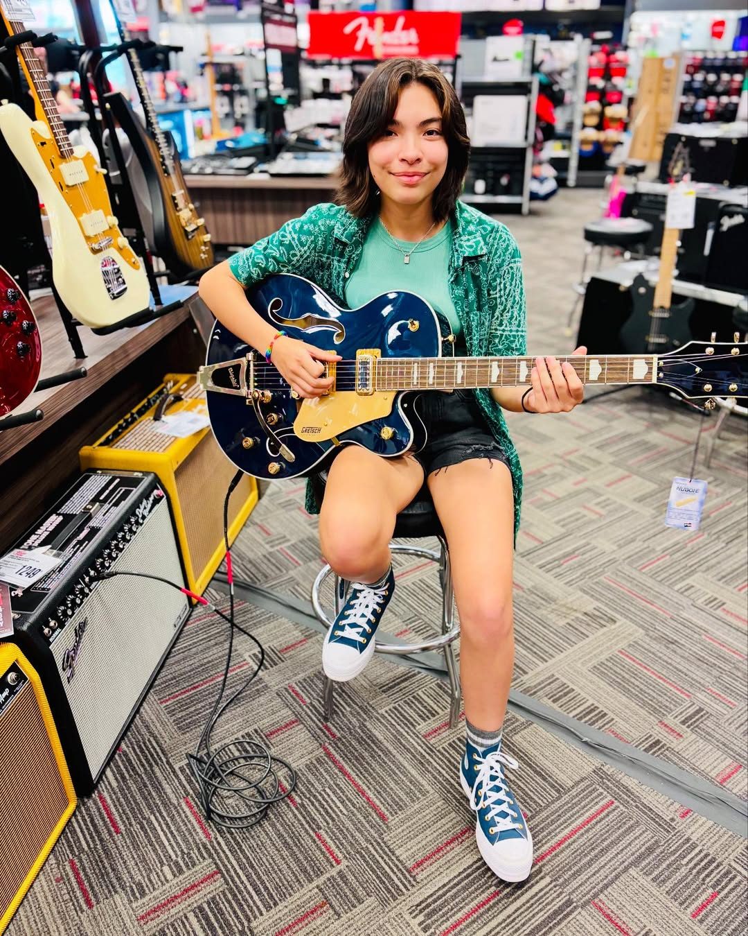 Ren seated in a music shop holding a blue guitar