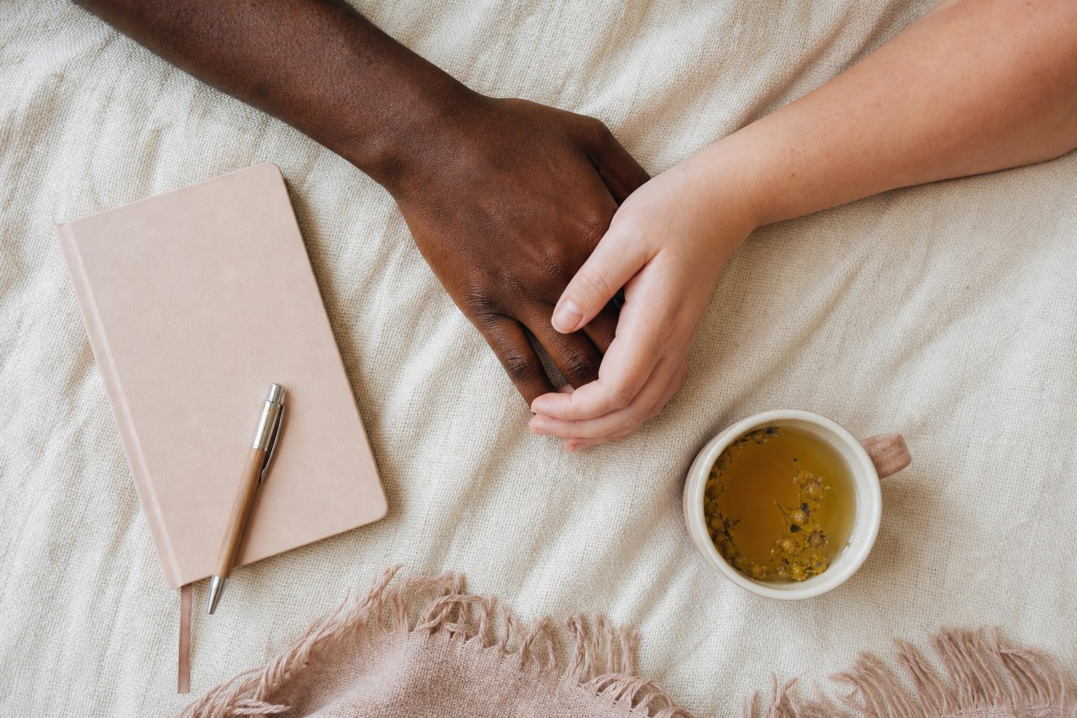Two hands resting together beside a notebook and herbal tea