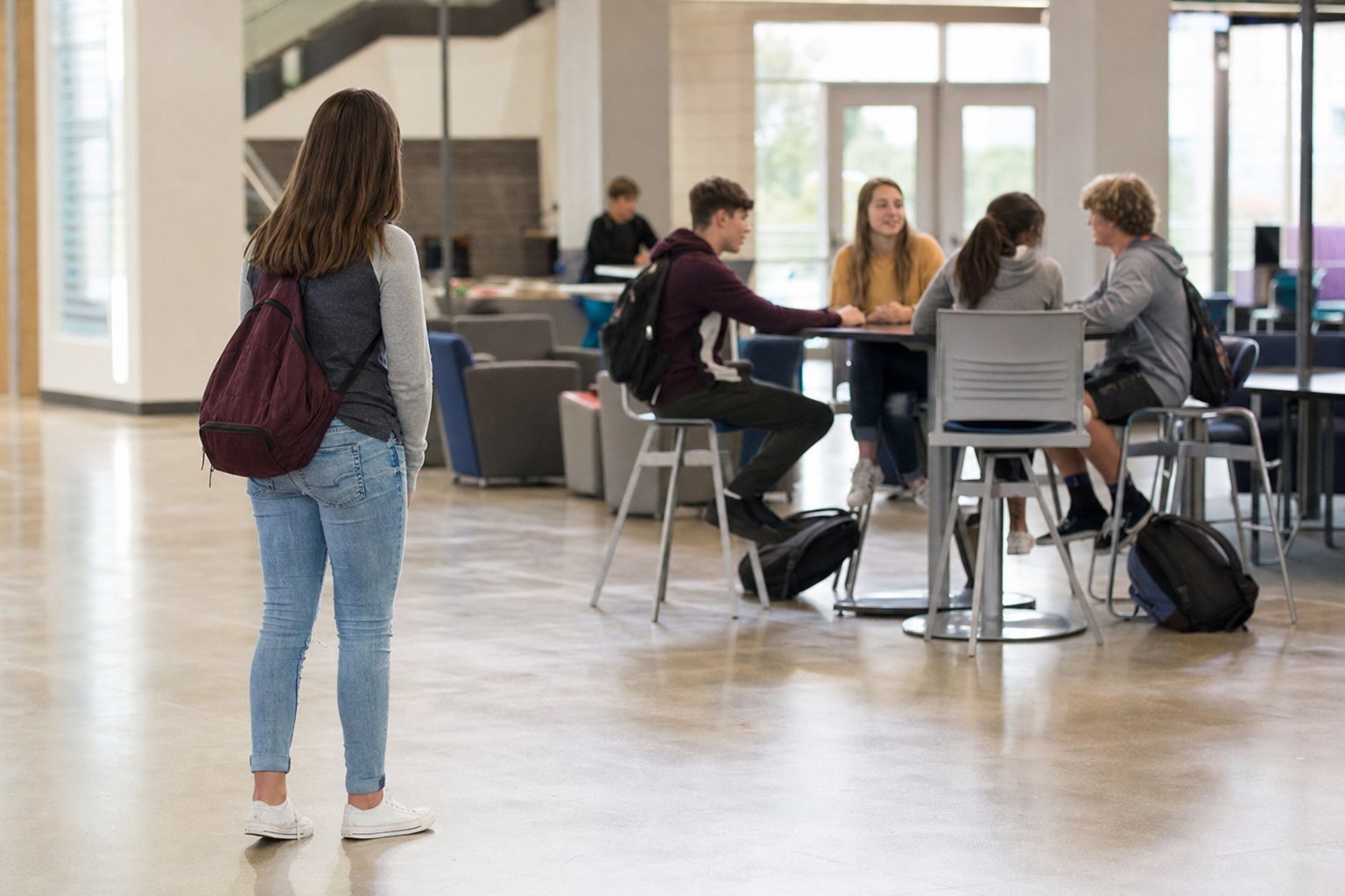 A high school student considering joining a small group of peers in a school common area.