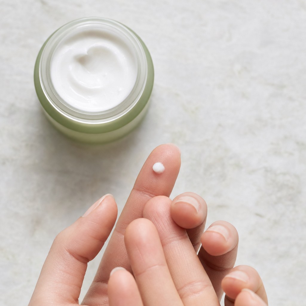 A small amount of eye cream on a fingertip beside an open cream jar