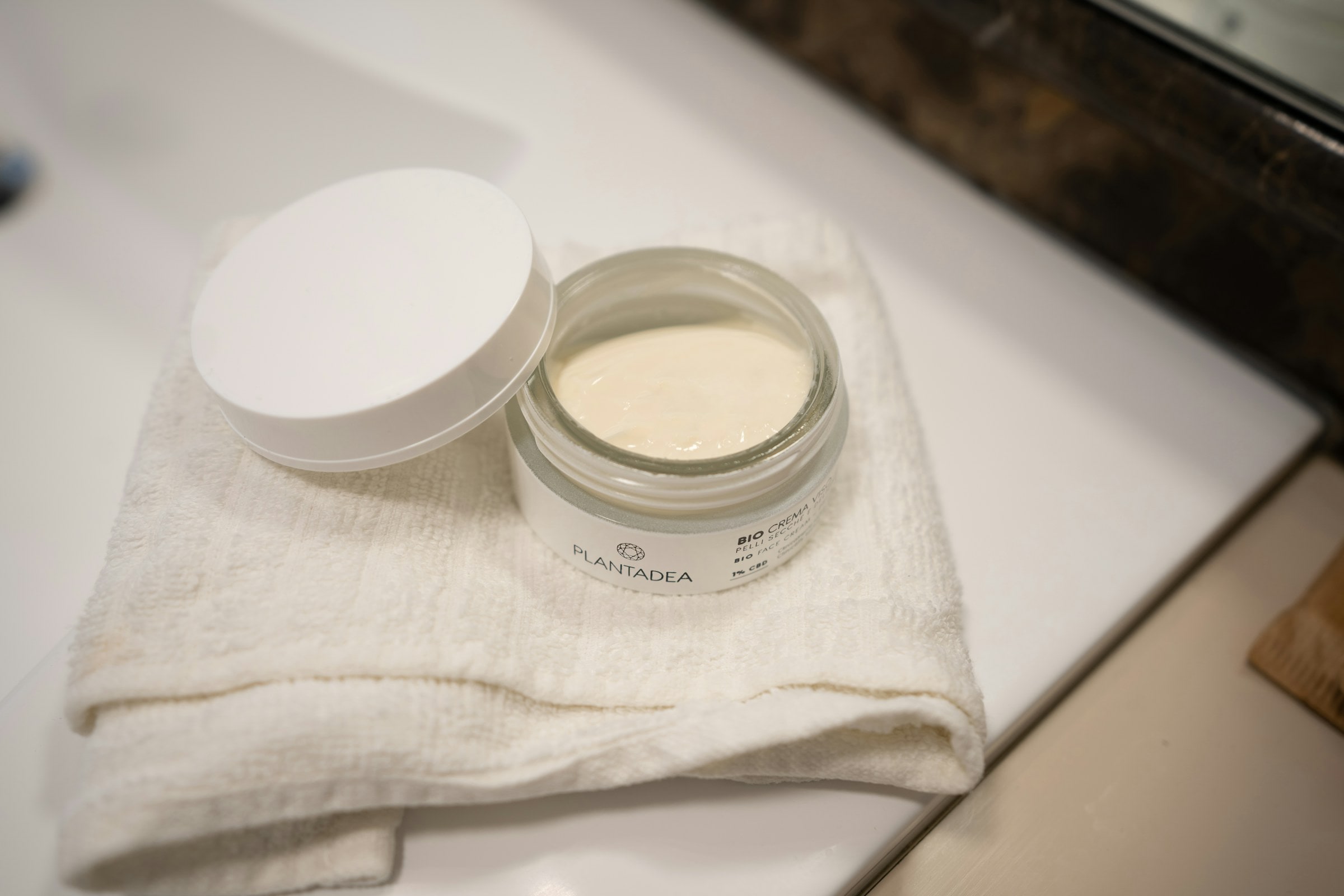 Open jar of cream resting on a white towel beside a bathroom sink