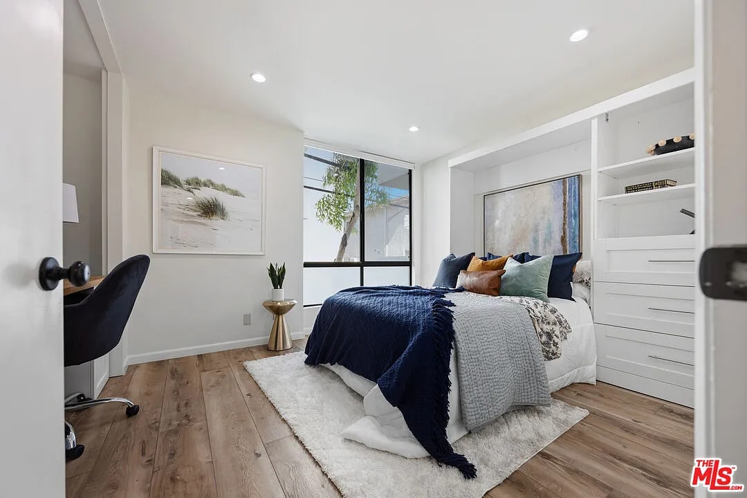 Staged bedroom with navy bedding, warm wood floors, and built-in shelving