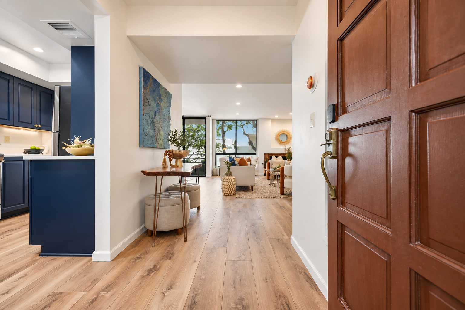 Staged entry with navy kitchen cabinetry, warm wood floors, and a view into the living space