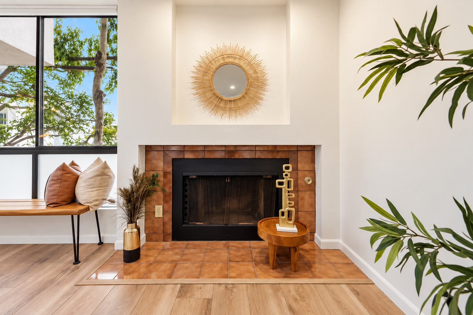 Staged living room with a warm terracotta tile fireplace and sunburst mirror
