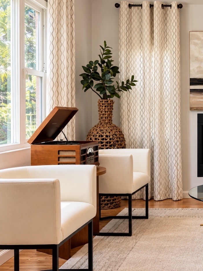 Warm staged sitting area with ivory chairs, a record player, and woven statement vase